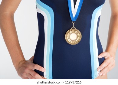 Middle Section Of An Olympic Swimmer's Body Wearing A Gold Medal And A Blue Sports Swimming Costume Against A White Background.