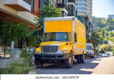 Middle Size Compact Yellow Rig Semi Truck Delivering Cargo In Box Truck Standing On The Street Parking Spot With Multilevel Buildings Waiting For Unloading Delivered Stuff