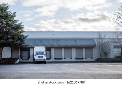 Middle white compact industrial rig semi truck with long box trailer for local routs standing in warehouse dock with multiply gates for loading commercial cargo for the next delivery