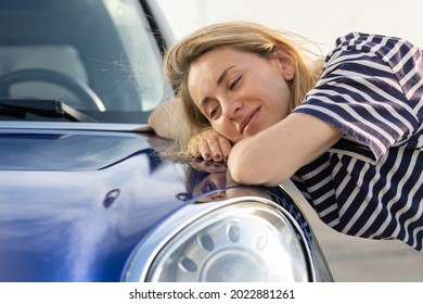 Middle woman driver dreaming, embracing hood of car after detailing, polishing. Happy female customer hugging lying on a bonnet of new blue automobile outdoors. Car insurance advertisement concept.