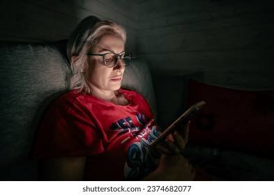 middleadged female sitting on bed and watching movie on mobile phone in dark bedroom in late evening - Powered by Shutterstock