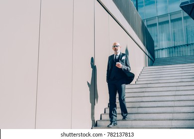 Middle-age contemporary businessman walking outdoor in the city, using smart phone hand hold - business, work, communication concept