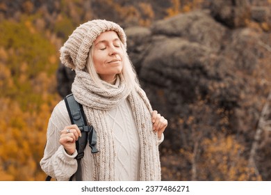 Middle-age happy smiling woman backpacker relaxation on top rocky mountains, with backpack, female breathing clean air with his eyes closed. Adventure, travel, holiday concept.