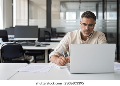 Middle-age Hispanic man using laptop computer for business studying, watch online virtual webinar training meeting, video call. Focused mature Indian or Latin businessman work in office, copy space. - Powered by Shutterstock
