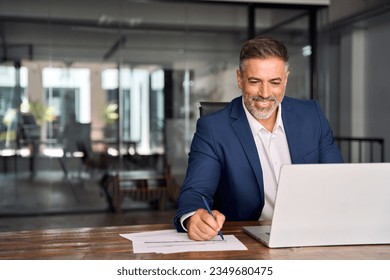 Middle-age Hispanic man using laptop computer for business studying, watch online financial webinar training meeting, video call. Focused mature Indian or Latin businessman work in office, copy space. - Powered by Shutterstock