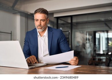 Middle-age Hispanic man using laptop computer for business studying, watch online financial webinar training meeting, video call. Focused mature Indian or Latin businessman work in office, copy space. - Powered by Shutterstock