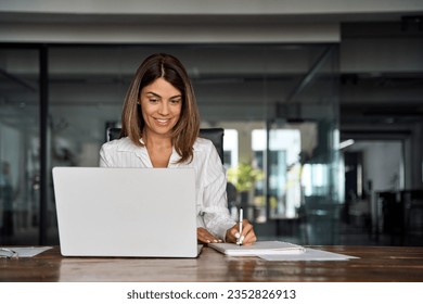 Middle-age Hispanic woman using laptop computer for business studying, watch online virtual webinar training meeting,video call. Focused mature 40s years Latin businesswoman work in office, copy space - Powered by Shutterstock