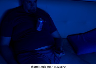 Middle-age, over-weight man watching TV alone in the dark, while balancing a beer can on his over-sized belly.