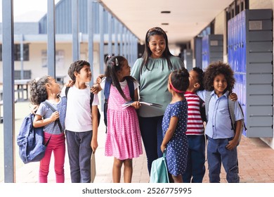 A middle-aged African American teacher with six diverse children outdoors at school. She holds tablet, wearing a green top and skirt, her hair styled simply, learning, education, unaltered - Powered by Shutterstock