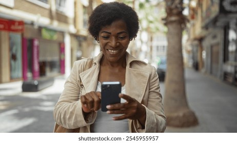 Middle-aged african american woman with curly hair using smartphone happily in an urban street - Powered by Shutterstock