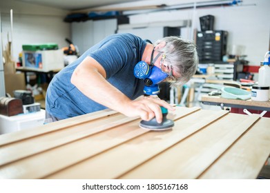 Middle-aged Artist With Dust Mask Sanding Wood In His Home Studio