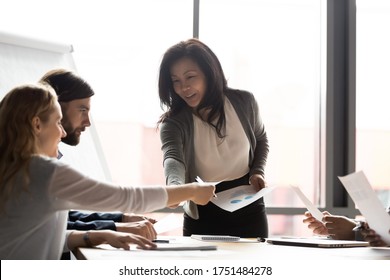 Middle-aged asian ethnicity woman coach or presenter during group meeting with investors or multiracial staff giving paper financials statistics handout materials data, seminar or negotiations concept