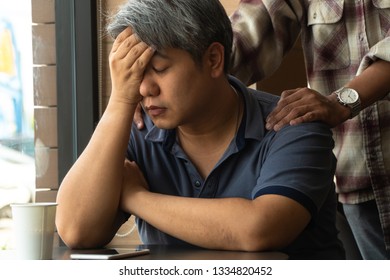 Middle-aged Asian Man 40 Years Old, Stressed And Tired, Are Sitting In Fast Food Restaurant And Have Friends Standing Behind To Encourage. Concept Of Helping And Encouraging