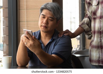 Middle-aged Asian man (40 years old), stressed and tired  and using smartphone, are sitting in fast food restaurant and have friends standing behind to encourage. Concept of helping and encouraging - Powered by Shutterstock