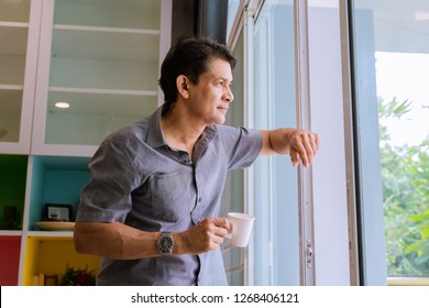 Middle-aged Asian man looking through a window, sipping coffee and using ideas - Powered by Shutterstock