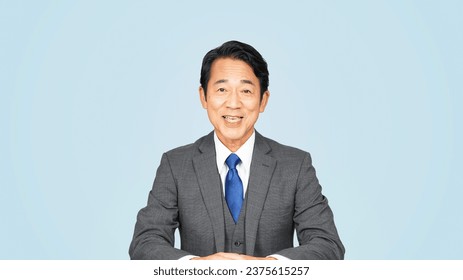 An middle-aged Asian man in a suit talking to the camera. announcer. news caster.