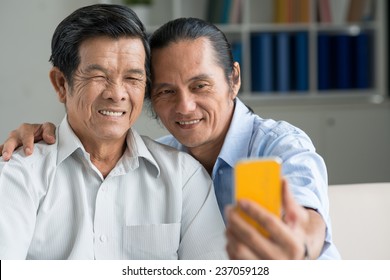 Middle-aged Asian Man Taking Selfie With His Senior Father