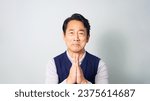 A middle-aged Asian man wearing casual wear apologizing in white background.
