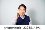 A middle-aged Asian man wearing casual wear asks for a favor while looking at the camera in front of a white background.