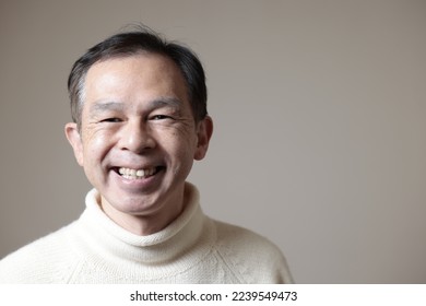 Middle-aged Asian man in white turtleneck wool sweater under gray background. Concept image of Warm Biz, stability in daily life, and sustainable living. - Powered by Shutterstock