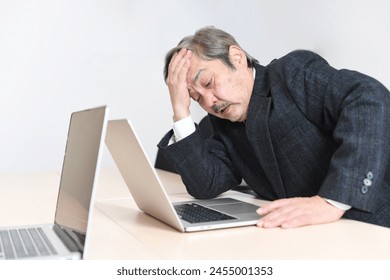 A middle-aged Asian office worker holding his head in front of a computer - Powered by Shutterstock