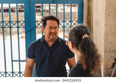 A middle-aged Asian woman berates her egotistical husband in front of their house, showing relationship challenges. - Powered by Shutterstock