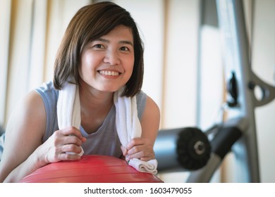 Middle-aged Asian Woman Smiling Brightly While Sitting At The Red Yoga Ball In The Gym