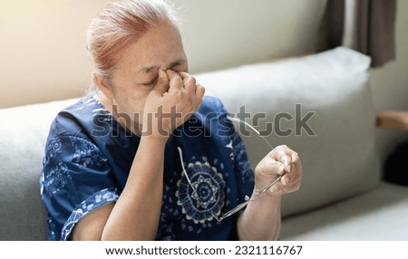 Middle-aged Asian woman taking off glasses closed eyes rubbing eyelid suffers from eye strain deterioration eyesight with age concept