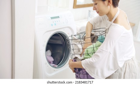 Middle-aged Asian Woman Using A Washing Machine.