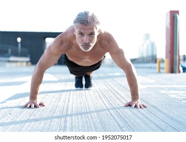 Middle-aged athletic man doing push ups outdoors. Fitness and exercising outdoors urban environment. - Powered by Shutterstock