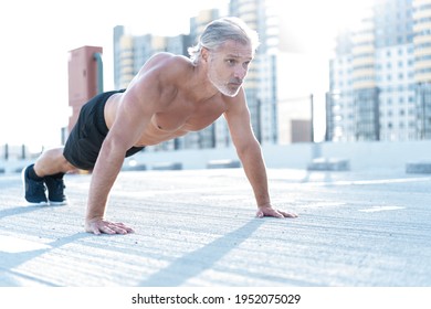 Middle-aged athletic man doing push ups outdoors. Fitness and exercising outdoors urban environment.