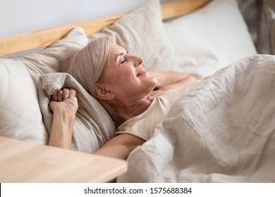 Middle-aged attractive woman lying in bed on comfortable memory foam pillow fresh beige color bed clothes enjoying early morning awakened at home closed eyes dreaming visualizing perfect day concept - Powered by Shutterstock