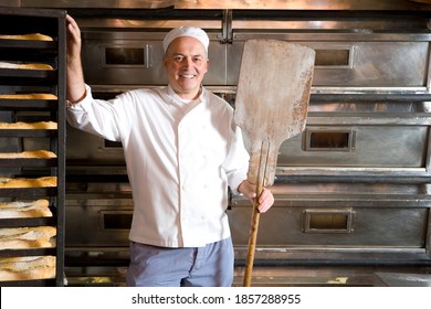 Middle-aged baker standing in his bakery with a wooden tray in his hand and smiling at the camera - Powered by Shutterstock