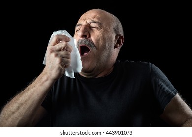 Middle-aged Balding Man With Seasonal Flu Or Allergy Sneezing Into A Handkerchief, Head And Shoulders Over A Black Background