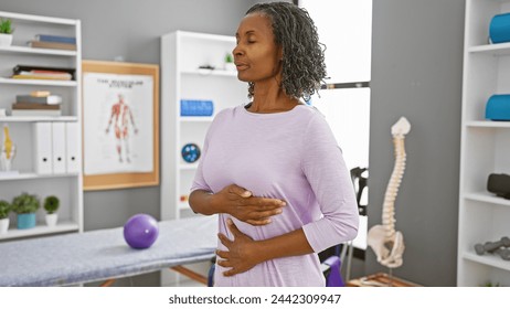 A middle-aged black woman practices breathing exercises at a rehab clinic, surrounded by therapeutic equipment. - Powered by Shutterstock