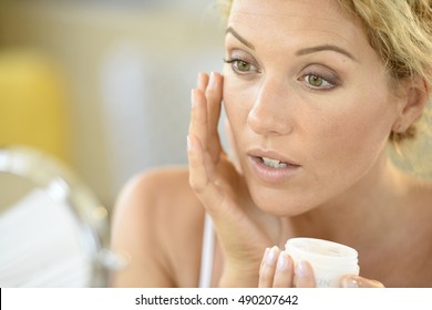 Middle-aged blond woman putting cosmetics on 