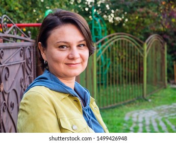 Middle-aged brunette woman at the gates of her country house in the village. Real people. Russia