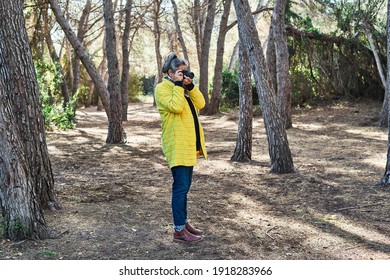 Middle-aged Brunette Woman With Gray Hair And Yellow Jacket, Takes Photos With Analog Reflex Camera In The Forest