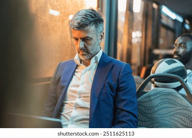 A middle-aged businessman in a blue suit intently working on his laptop while commuting on a bus at night. - Powered by Shutterstock