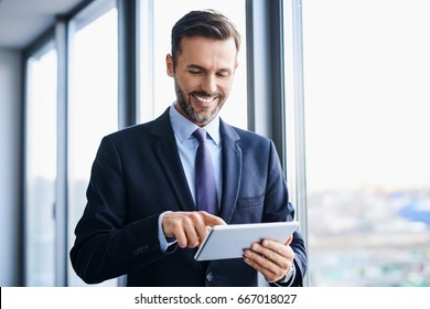 Middle-aged businessman using tablet while standing in office