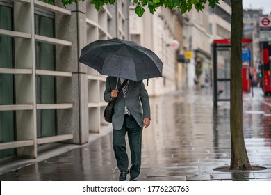 Middle-aged businessman wearing a suit caught out in the rain during a windy  drizzly day fighting the wind under an umbrella in Holborn, London during the COVID-19 pandemic 101 - Powered by Shutterstock