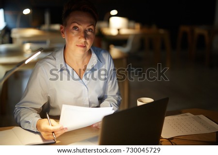 Middle-aged businesswoman with papers working overtime in office