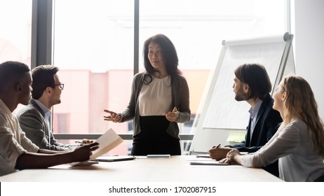 Middle-aged Businesswoman Stand Lead Team Meeting With Diverse Multiracial Colleagues In Office, Motivated Asian Female CEO Or Boss Talk At Briefing With Diverse Coworkers, Leadership Concept