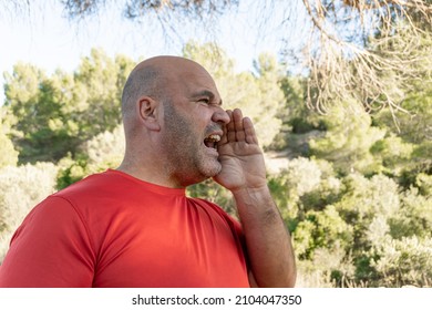 Middle-aged Caucasian Man With A Hand Over His Mouth Screaming In The Woods For Help