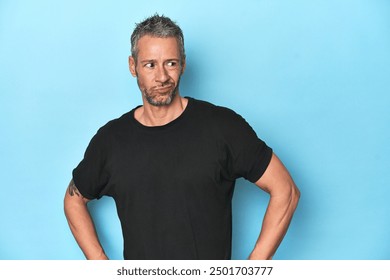 Middle-aged caucasian man on blue backdrop confused, feels doubtful and unsure. - Powered by Shutterstock