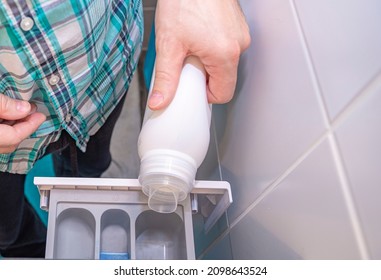A middle-aged Caucasian man pours bleach into the washing machine for washing clothes. - Shutterstock ID 2098643524