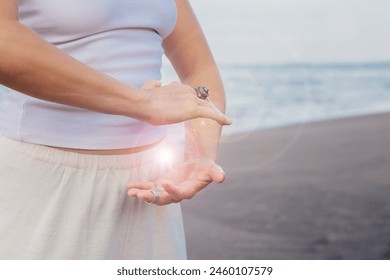 A middle-aged caucasian woman practices qigong energy exercise outdoor on the beach, blue sky and ocean backdrop, charges life force energy, esoteric practitioner, energy healer, grounding healing - Powered by Shutterstock