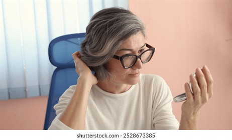 Middle-aged Caucasian woman smiles, adjusting short gray hair, wearing white top. - Powered by Shutterstock