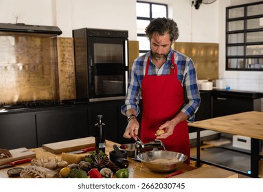 Middle-aged cook cracking egg and turning pasta dough by hand-crank roller on prep table in kitchen. Culinary, gourmet, rustic, artisan, craft, home cooking, food preparation