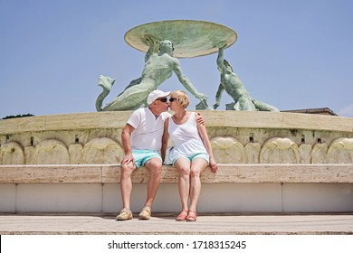 Middle-aged Couple Of Baby Boomers People Posing For Photograph Opposite Famous Fountain In Valletta In Malta On Sunny Summer Day. Travel Boom After End Of Coronavirus Concept